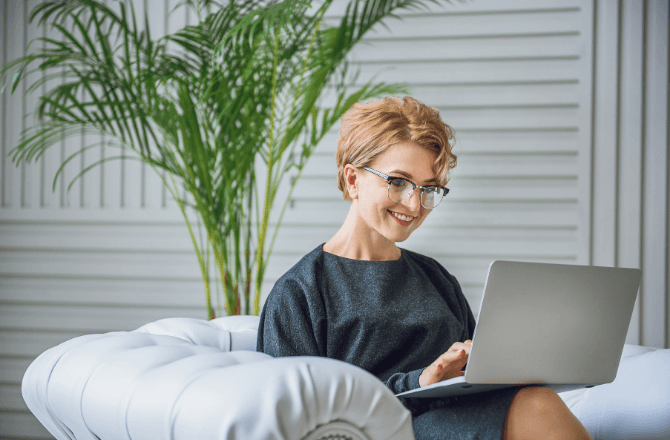 Happy woman sitting on couch using laptop