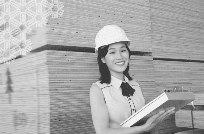 Woman wearing hard hat and holding clipboard in a lumber warehouse