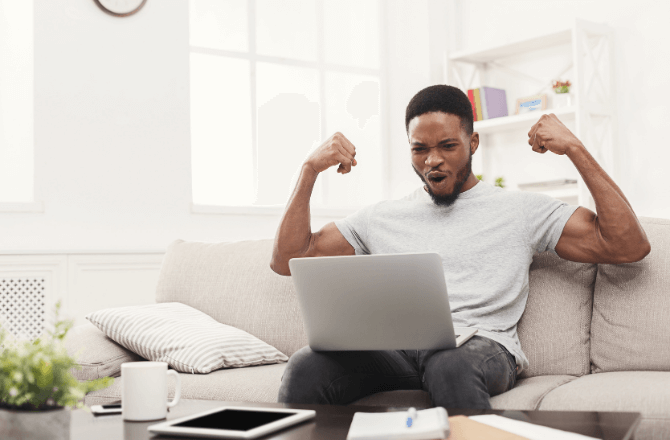 Man flexing his arms with excited expression on his face, looking at his open laptop