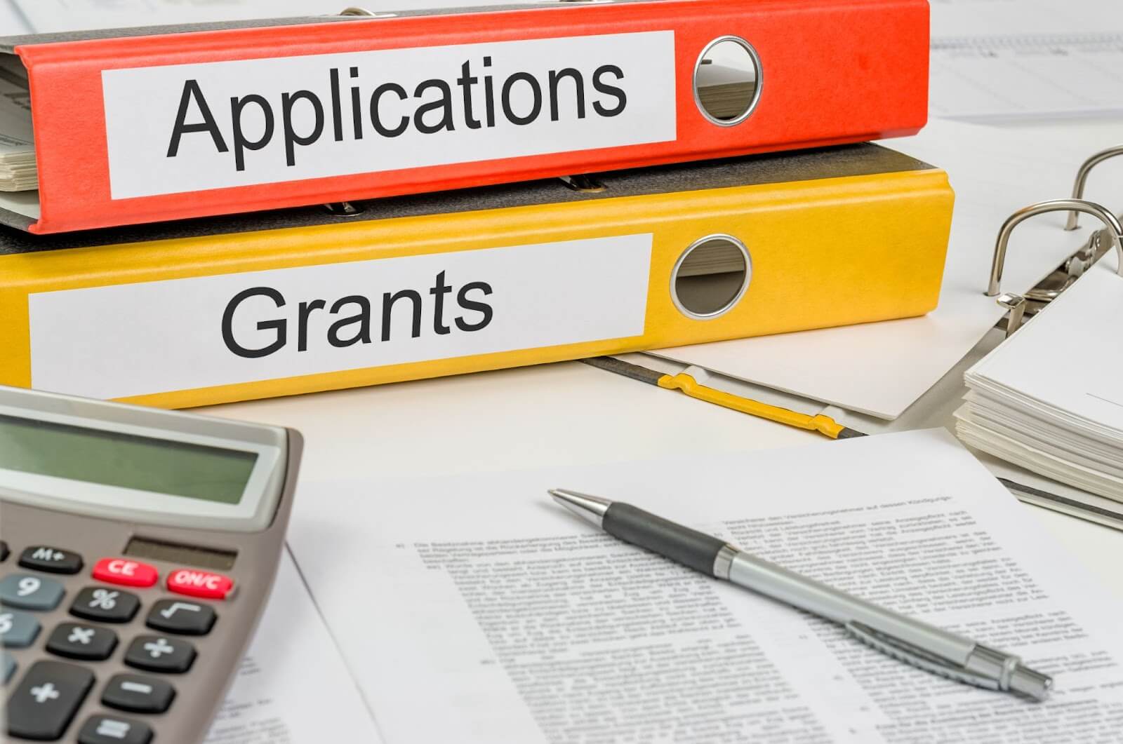 Orange binder with a label that says "Applications" and yellow binder with a label that says "Grants"