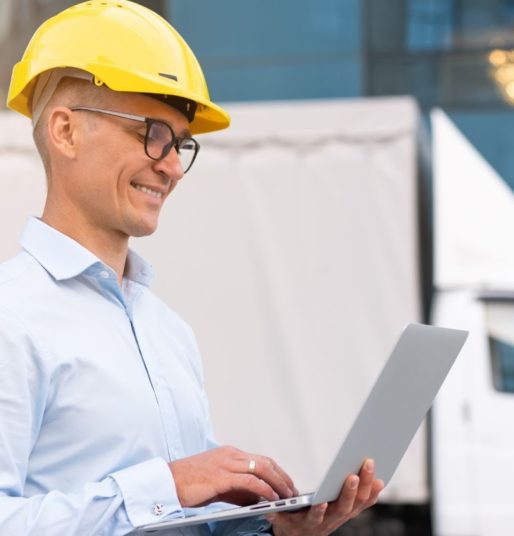 Trucking manager standing outside next to box truck, holding laptop and looking at screen