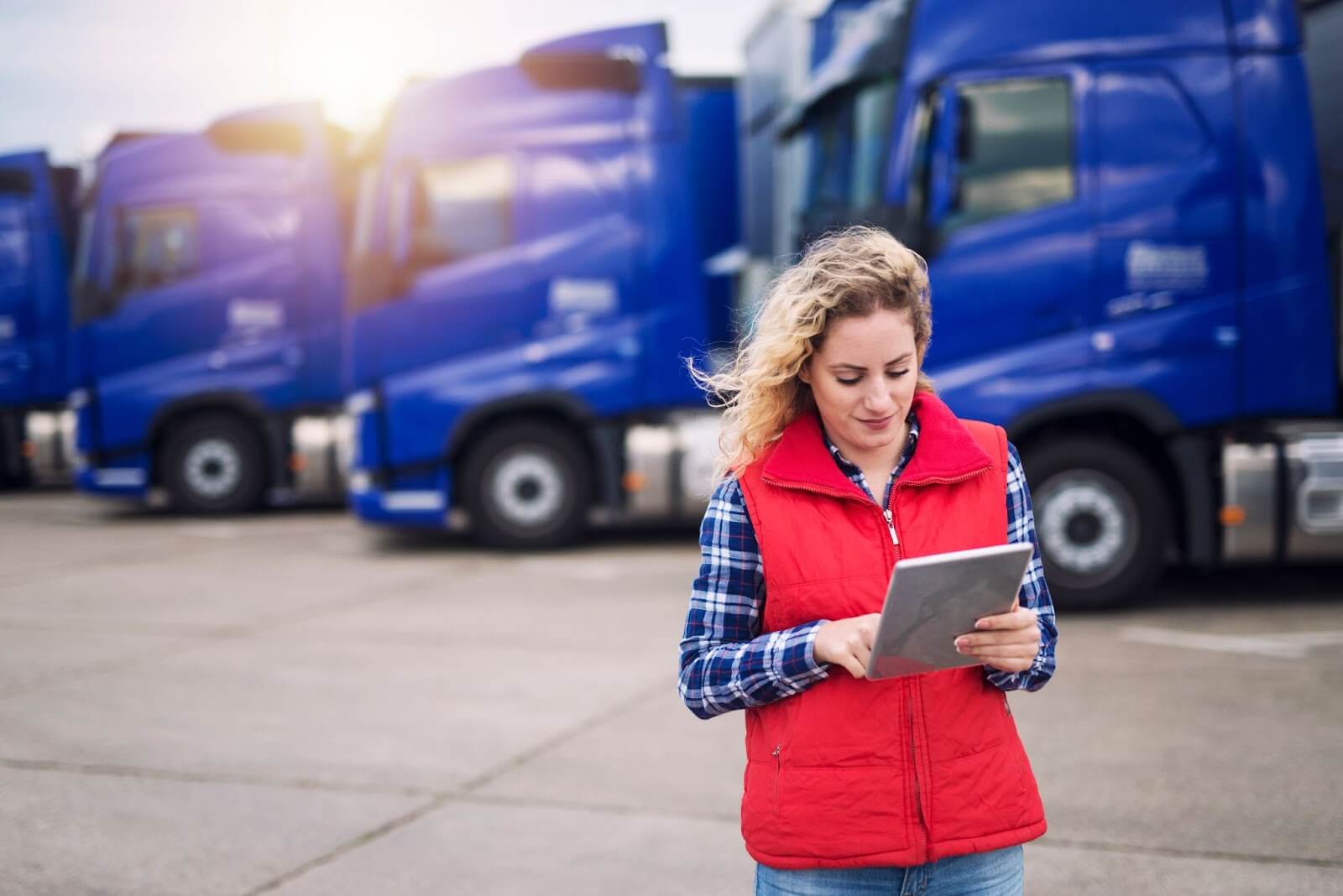 Woman interacting with tablet while standing in front of several parked semi-trucks